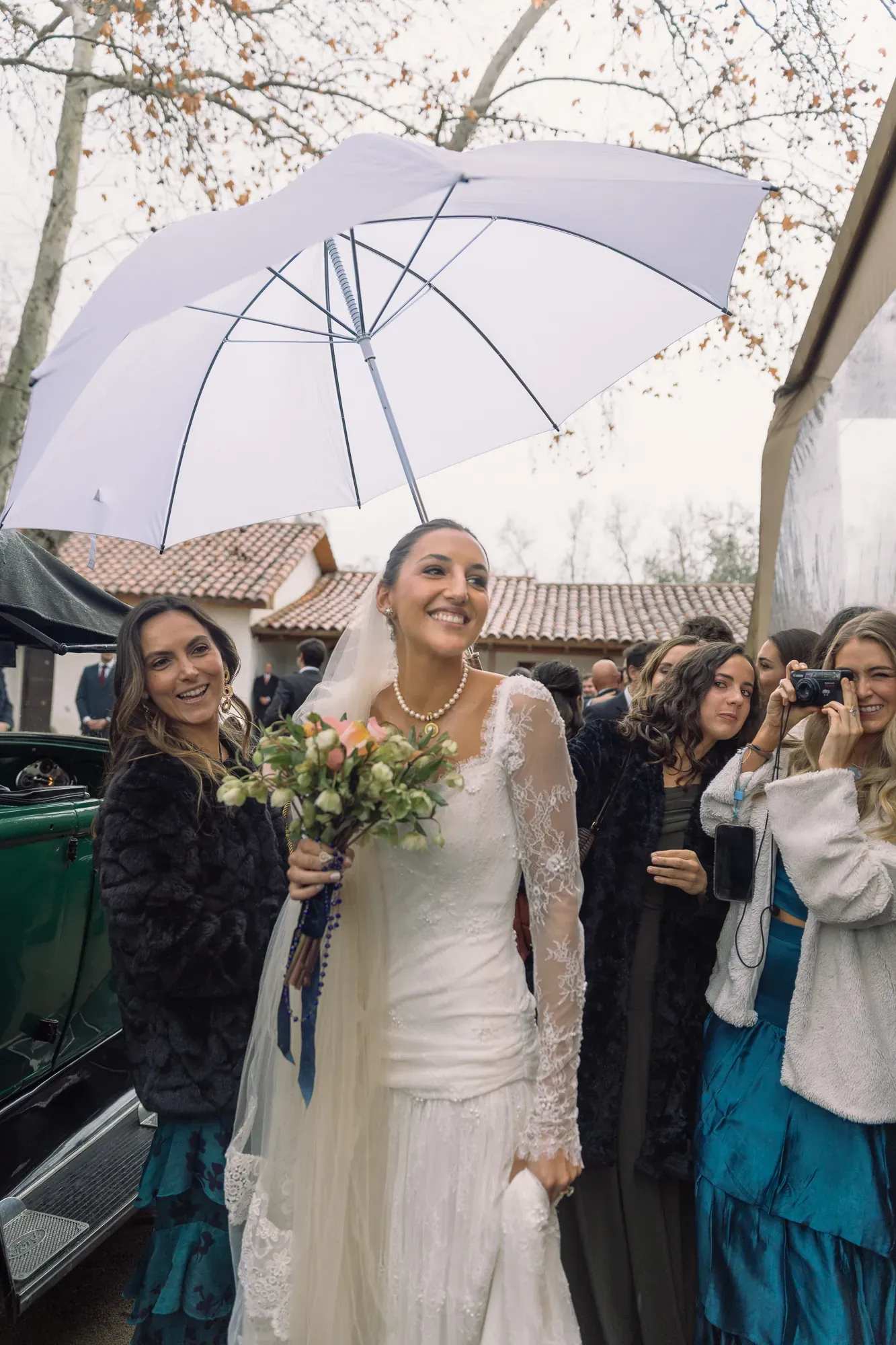La novia sonríe bajo un paraguas blanco, entre sus amigas