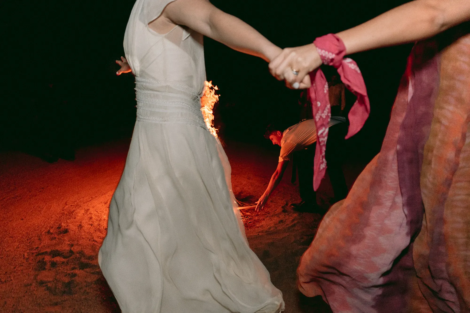 Dos manos se toman en medio del baile, de noche, junto al fuego